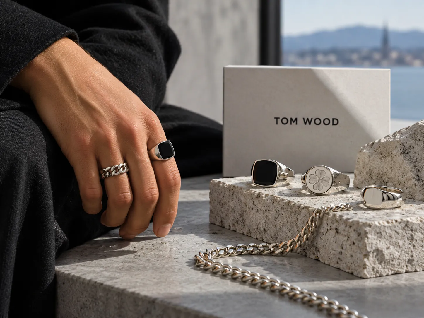 Tom Wood silver rings and chain displayed on stone beside a model's hand